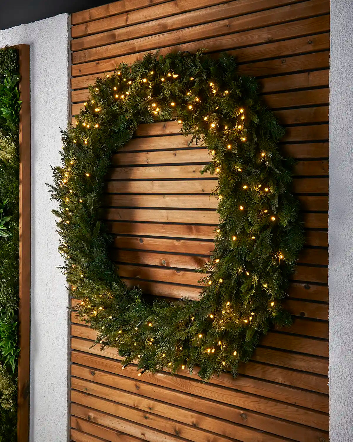 1.2m pre-lit natural fir wreath displayed outdoors on a wooden feature wall.