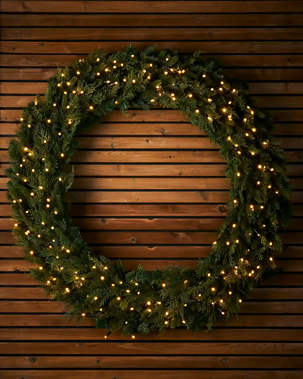 1.2m pre-lit natural fir wreath with warm white LEDs on a wooden wall.