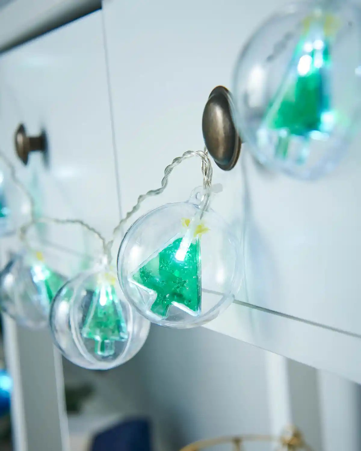 Christmas tree bauble LED string lights displayed along a white mantel with festive décor