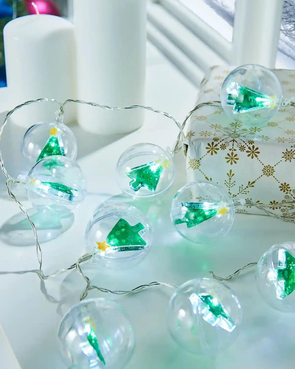 Christmas tree bauble LED string lights styled on a white table beside candles and wrapped gifts