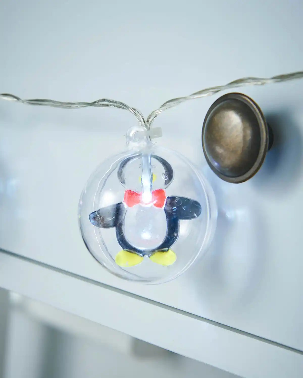 Close-up of a clear penguin bauble with bright white LED light on a 1.8 m string light