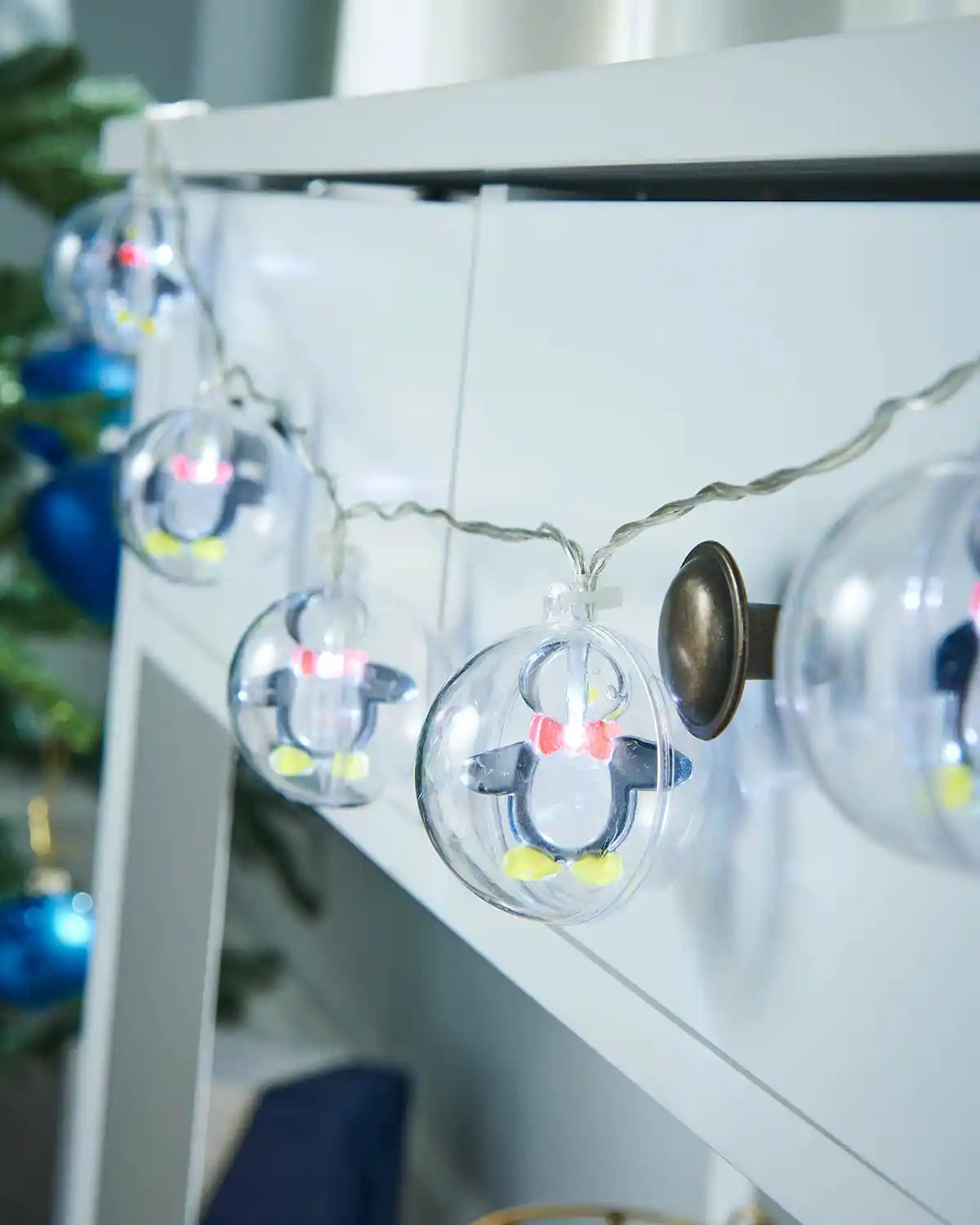 Penguin bauble LED string lights displayed along a white mantel with festive décor