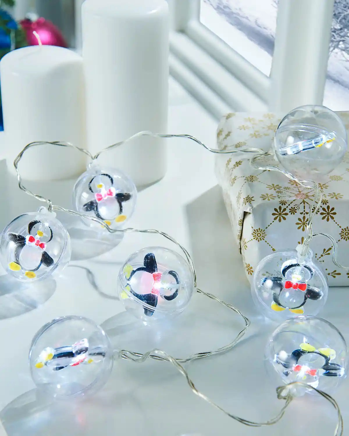 Penguin bauble LED string lights styled on a white table beside candles and wrapped gifts