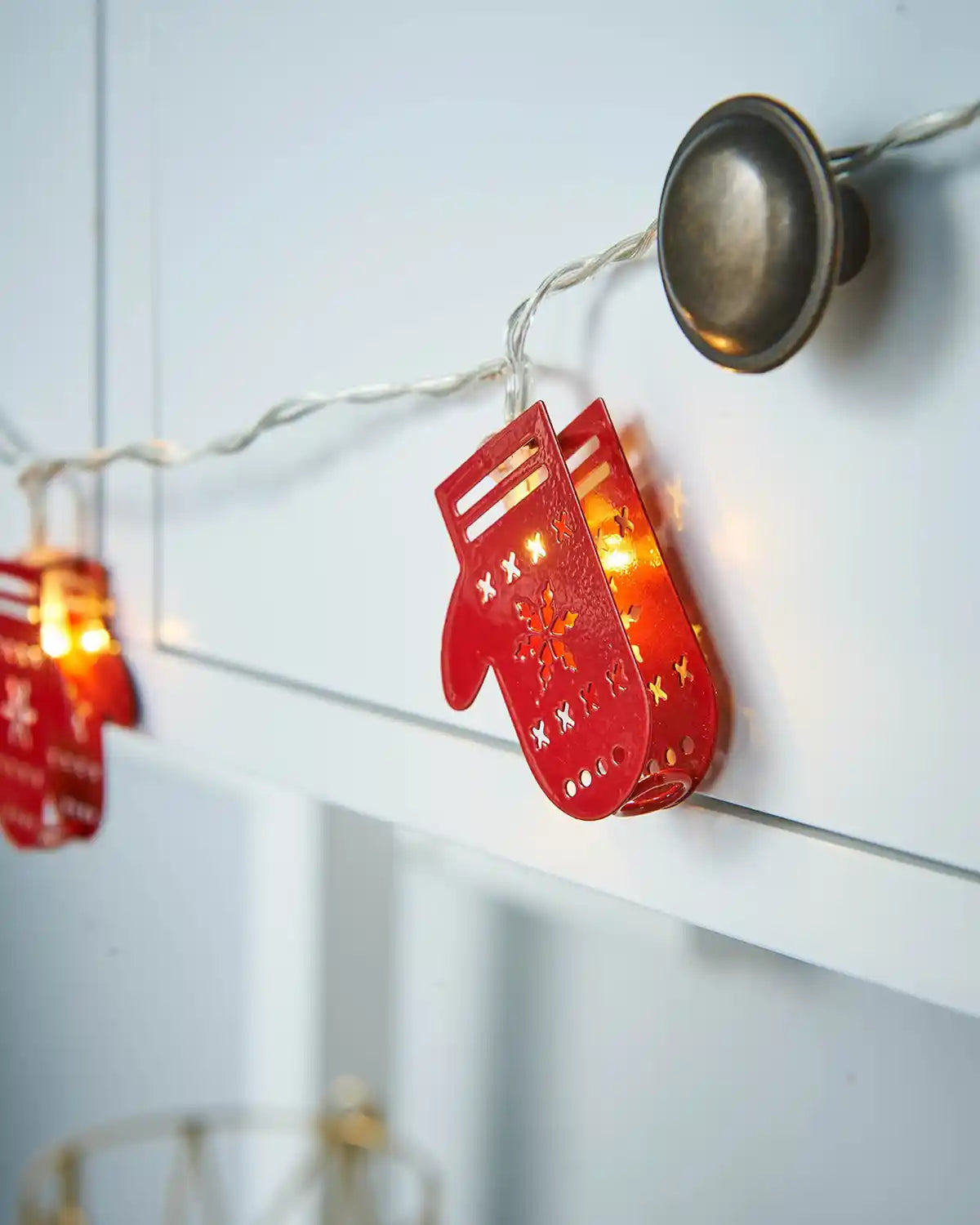 Close-up of red Santa glove LED string lights hanging from a white mantel