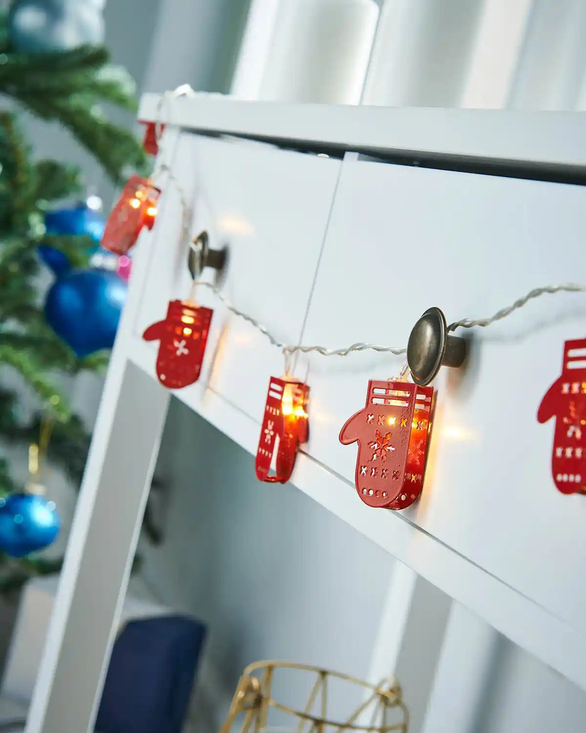 Santa gloves LED string lights draped along a white mantel with festive décor