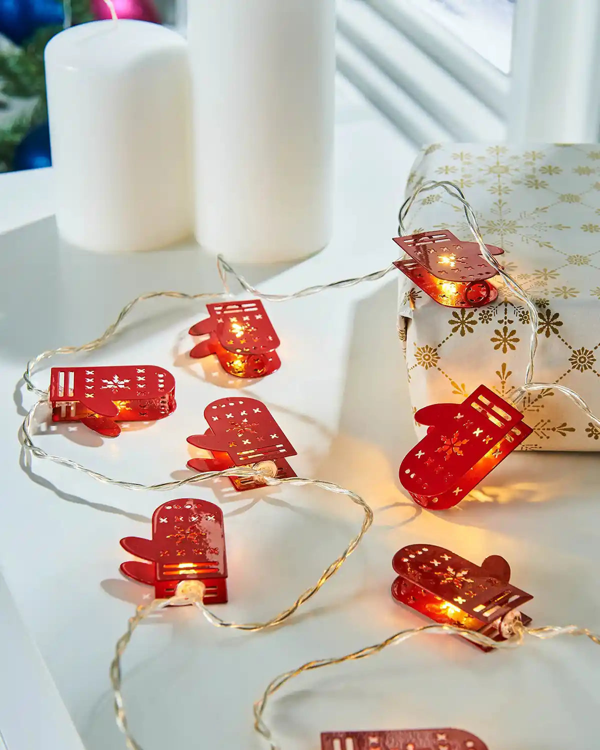 Santa gloves LED string lights styled on a white table beside candles and a wrapped gift