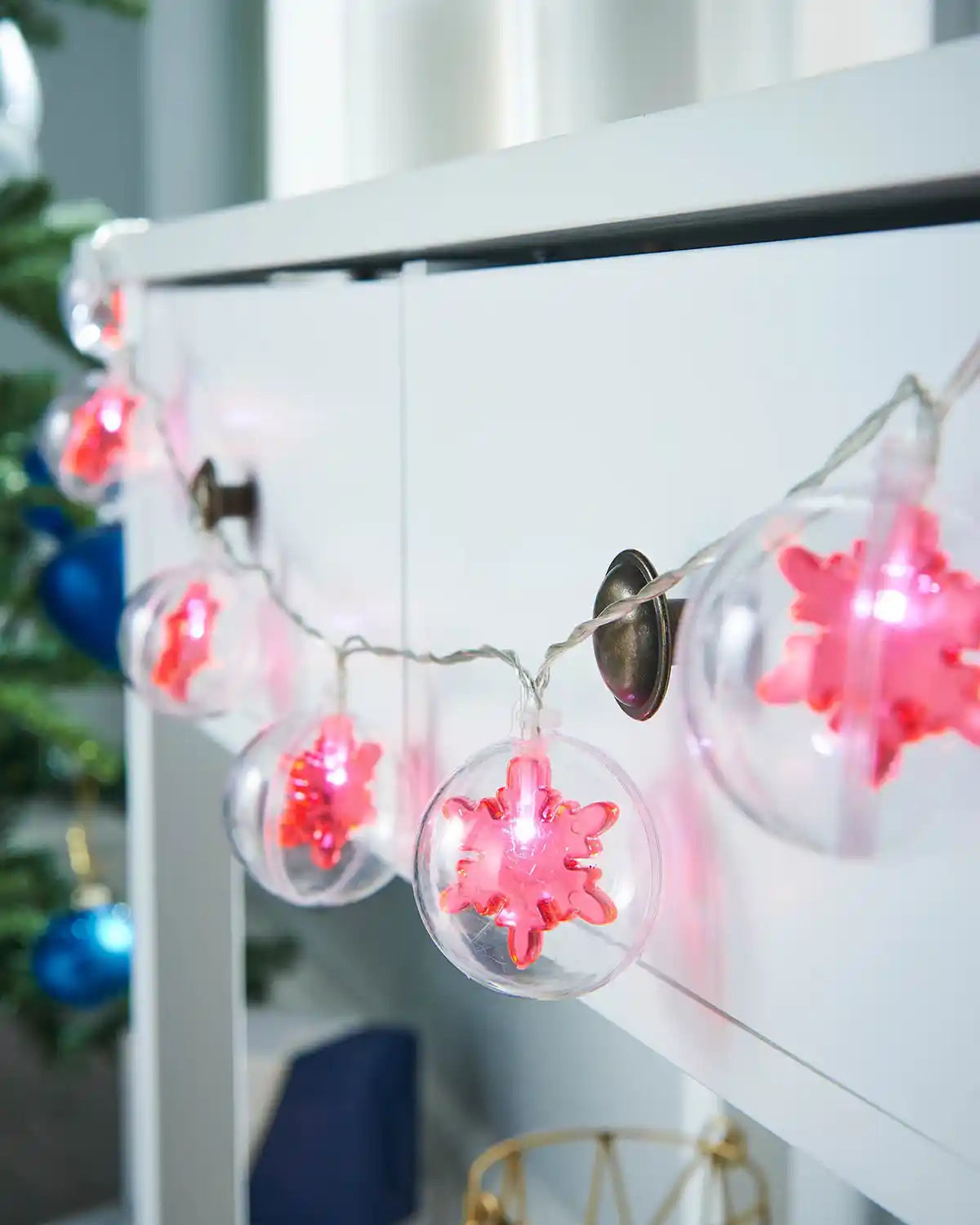 Red snowflake bauble LED string lights displayed along a white mantel with festive décor