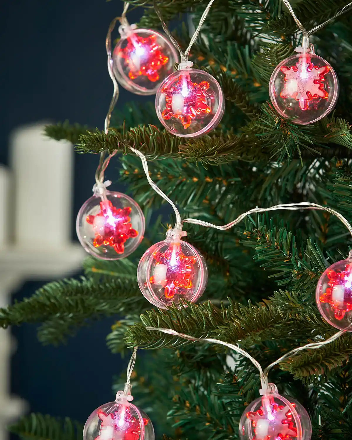 Red snowflake bauble LED string lights hanging on a Christmas tree