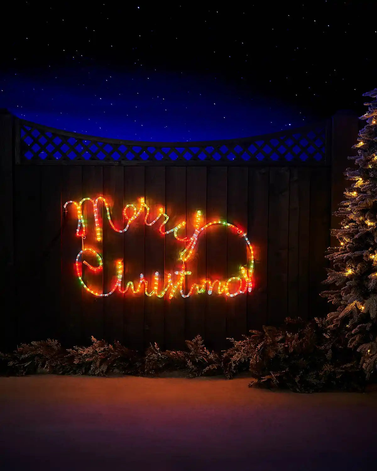 100 cm multi-coloured Merry Christmas rope light displayed outdoors beside a lit tree