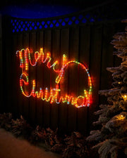 Multi-coloured Merry Christmas rope light display on a garden fence at night
