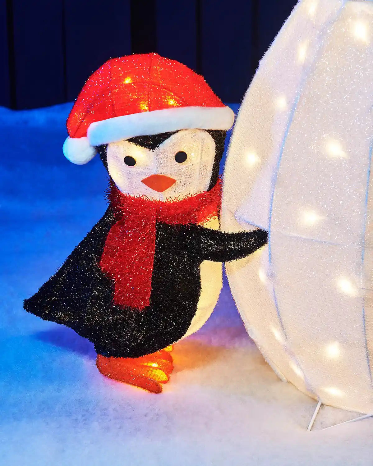 Close-up of a pre-lit penguin wearing a red Santa hat and scarf beside the snowman.