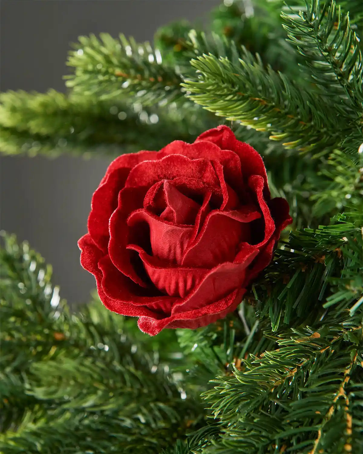 A 10cm red artificial rose flower attached to a Christmas tree in front of a grey wall background