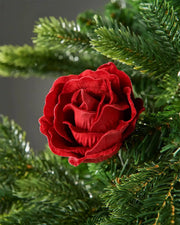 A 10cm red artificial rose flower attached to a Christmas tree in front of a grey wall background
