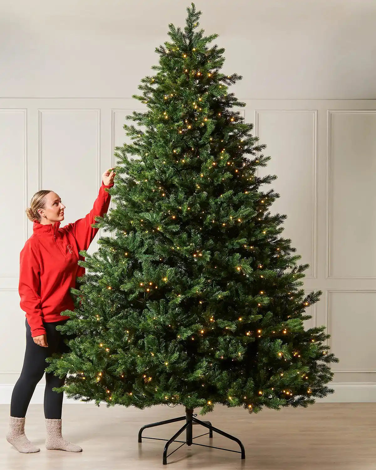 10ft pre-lit balsam fir Christmas tree with warm white LED lights, shown indoors with a person standing beside it for scale.