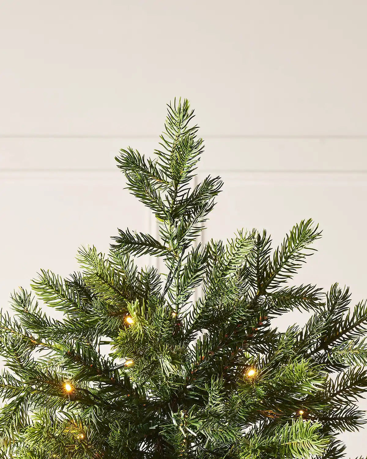 Detail of the top section of the 10ft pre-lit balsam fir Christmas tree with realistic tips and warm white LED lights.