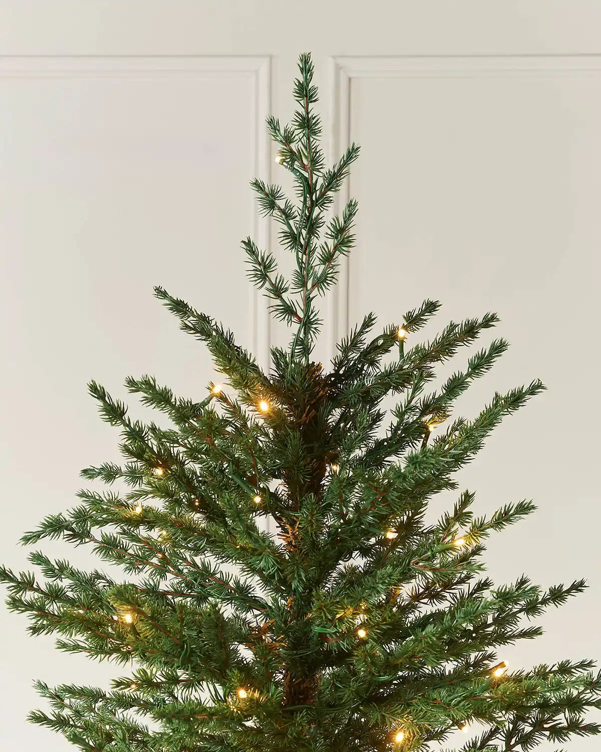 Top section of the 10ft pre-lit Traditional Fir Christmas tree showing slim green branches and warm white LEDs.