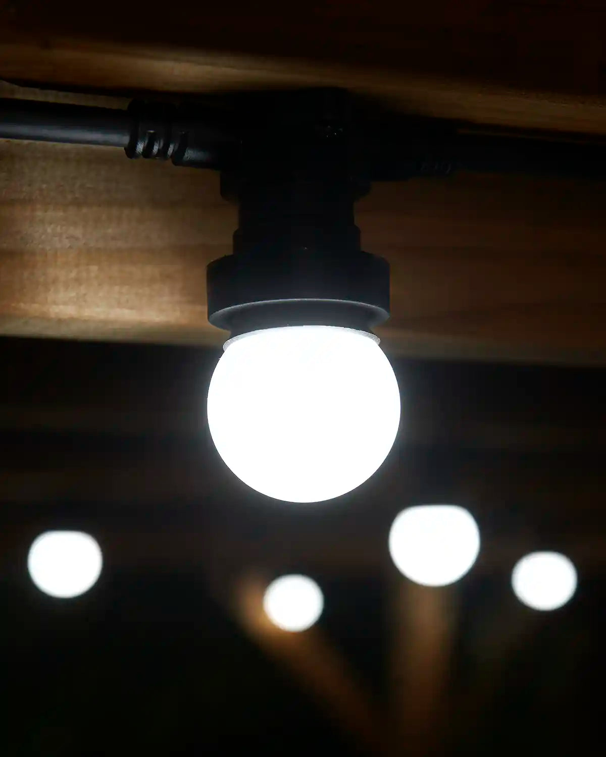White festoon bulb fitted to a black E27 socket beneath a wooden pergola.