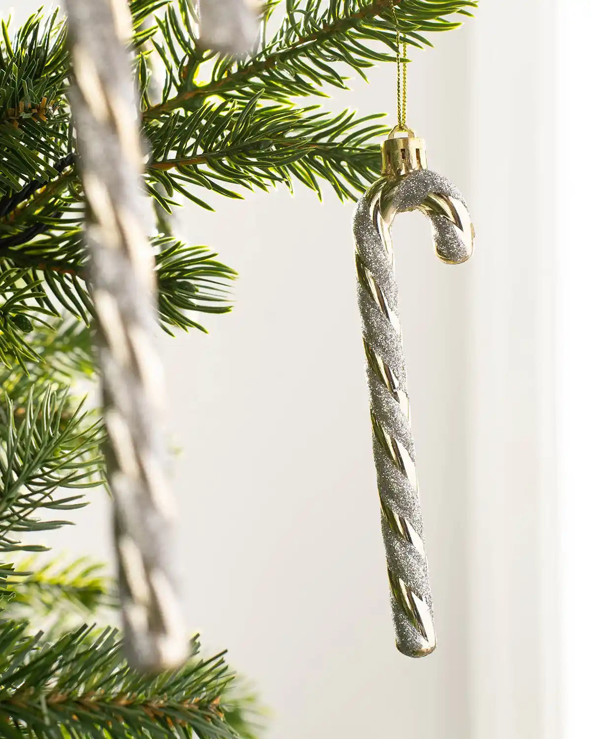 Gold and white shatterproof candy cane baubles displayed on Christmas tree branches