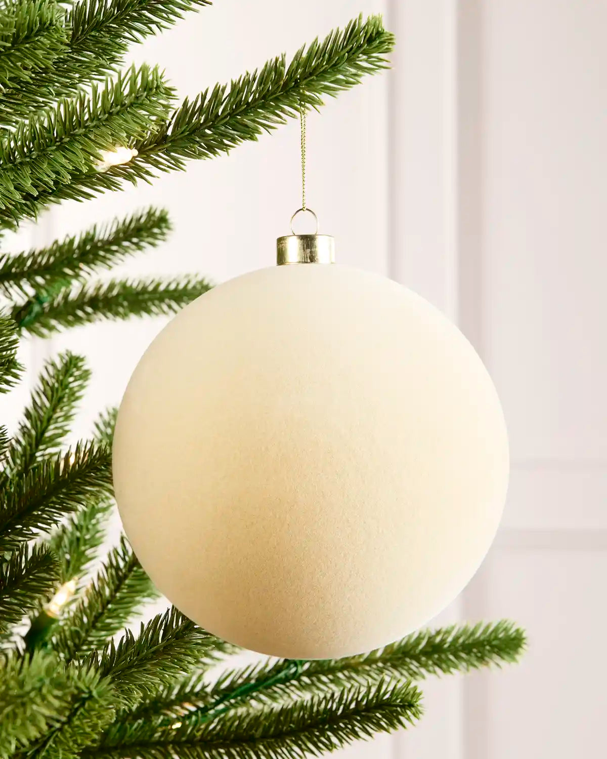 15 cm latte oversized velvet traditional bauble hanging from a Christmas tree with a gold cap.
