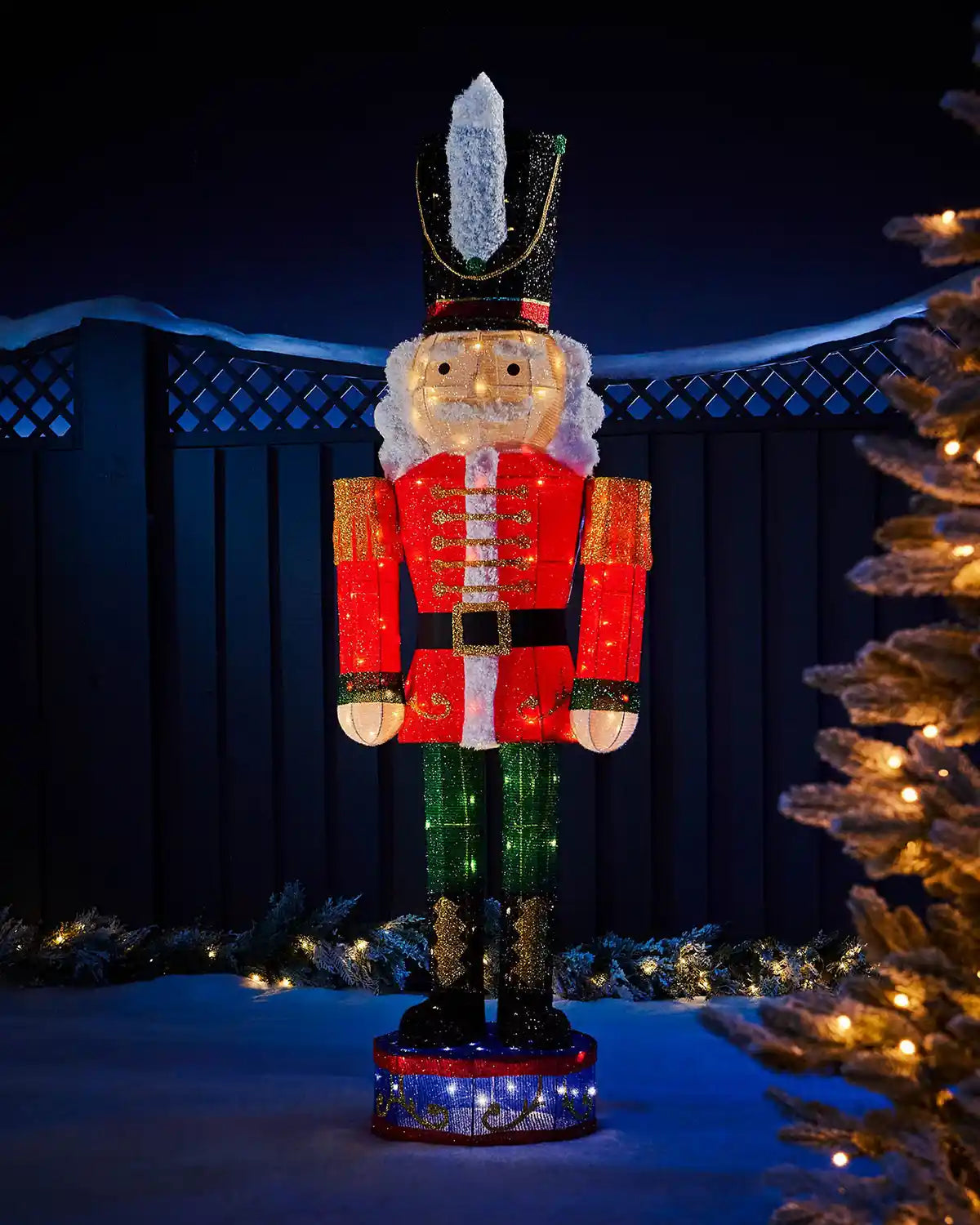 165cm pre-lit 3D nutcracker silhouette glowing in an outdoor Christmas display with festive trees and garland.
