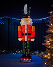 165cm pre-lit 3D nutcracker silhouette glowing in an outdoor Christmas display with festive trees and garland.