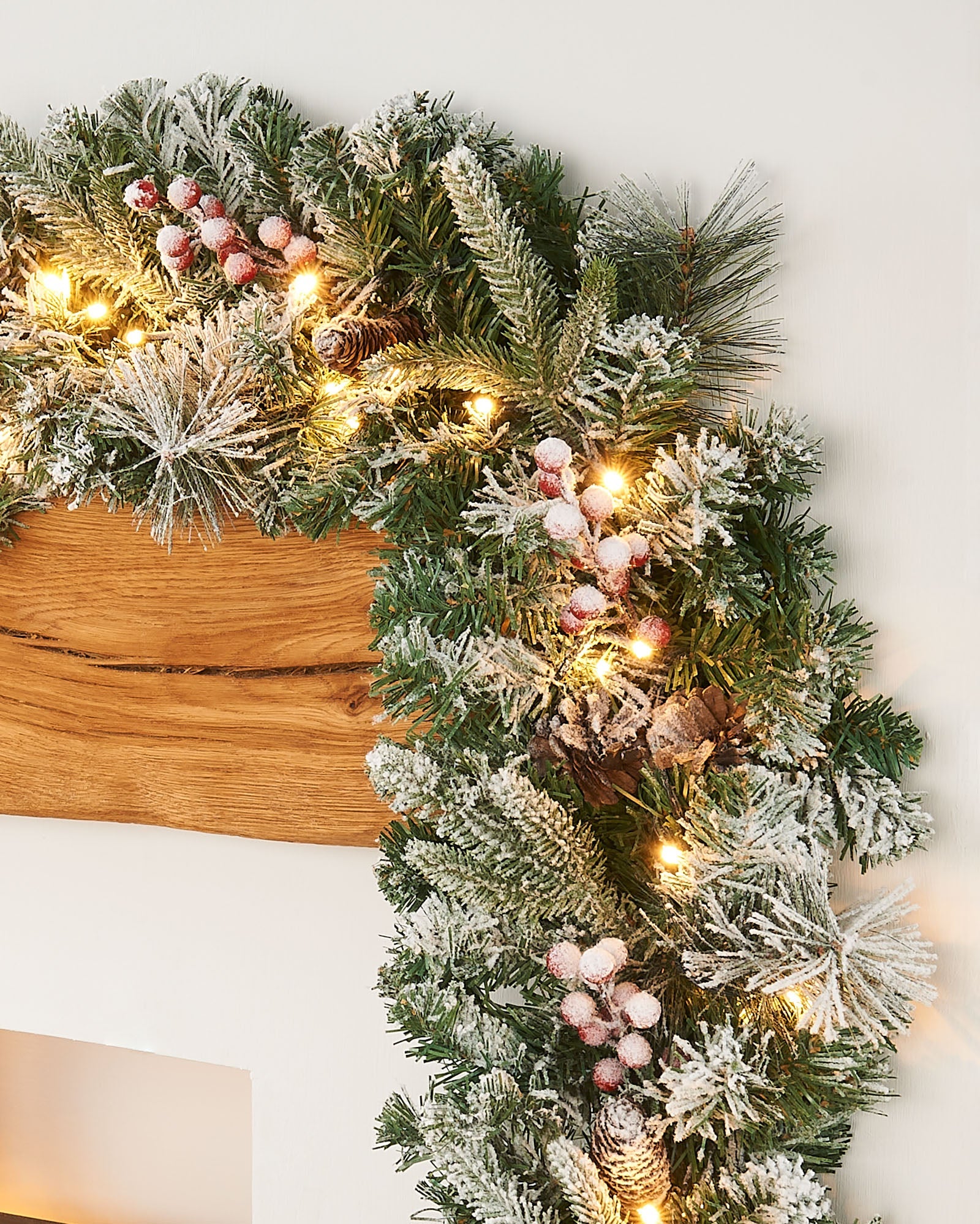 A festive Christmas garland with snow flock, pinecones, and berries, illuminated by warm white LED lights.