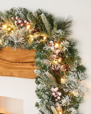 A festive Christmas garland with snow flock, pinecones, and berries, illuminated by warm white LED lights.