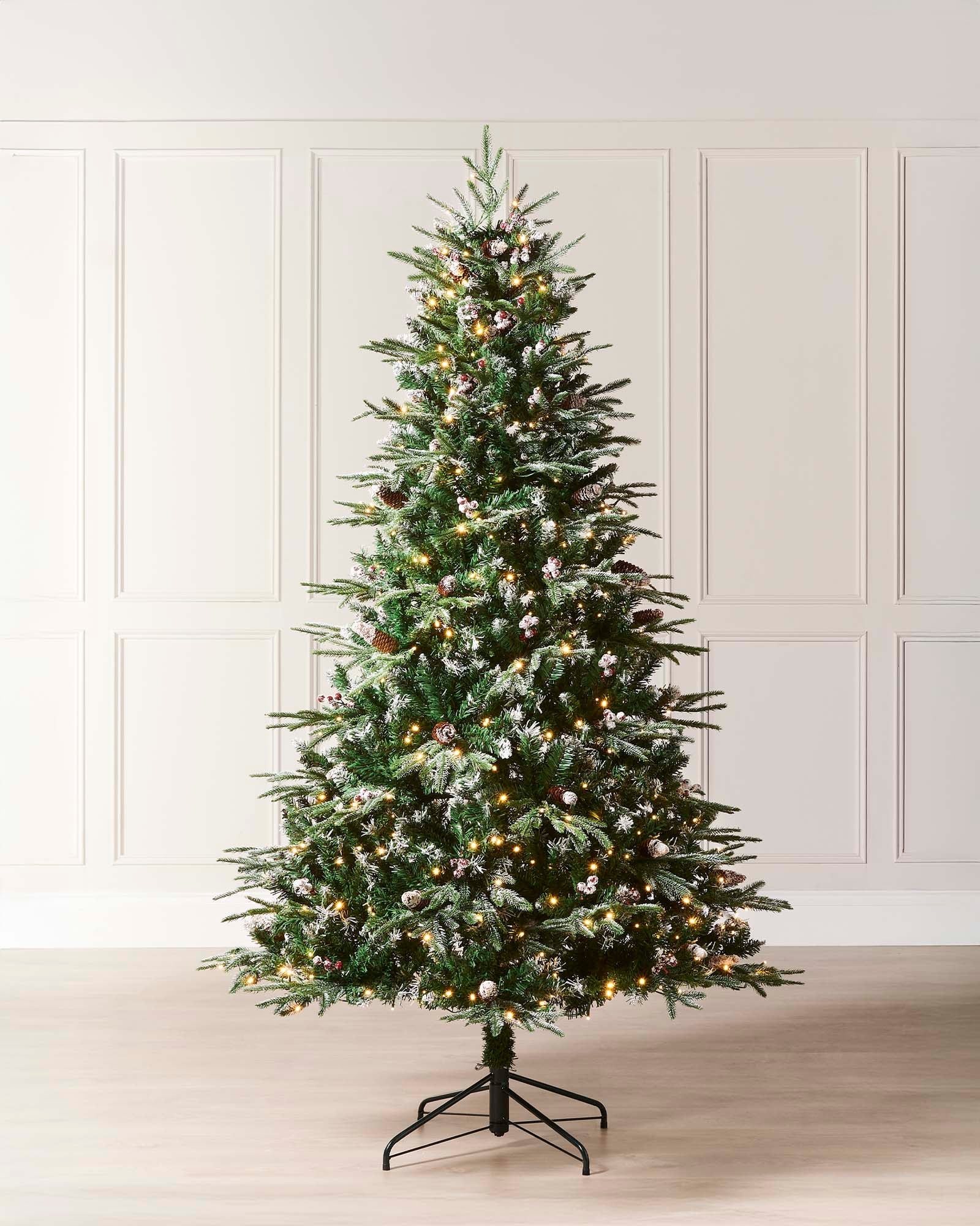 Pre-lit frosted Norwegian Spruce Christmas tree with snow-dusted branches, natural pinecones, and red berries. Features warm white multi-function LED lights and a lifelike PE and PVC tip construction.