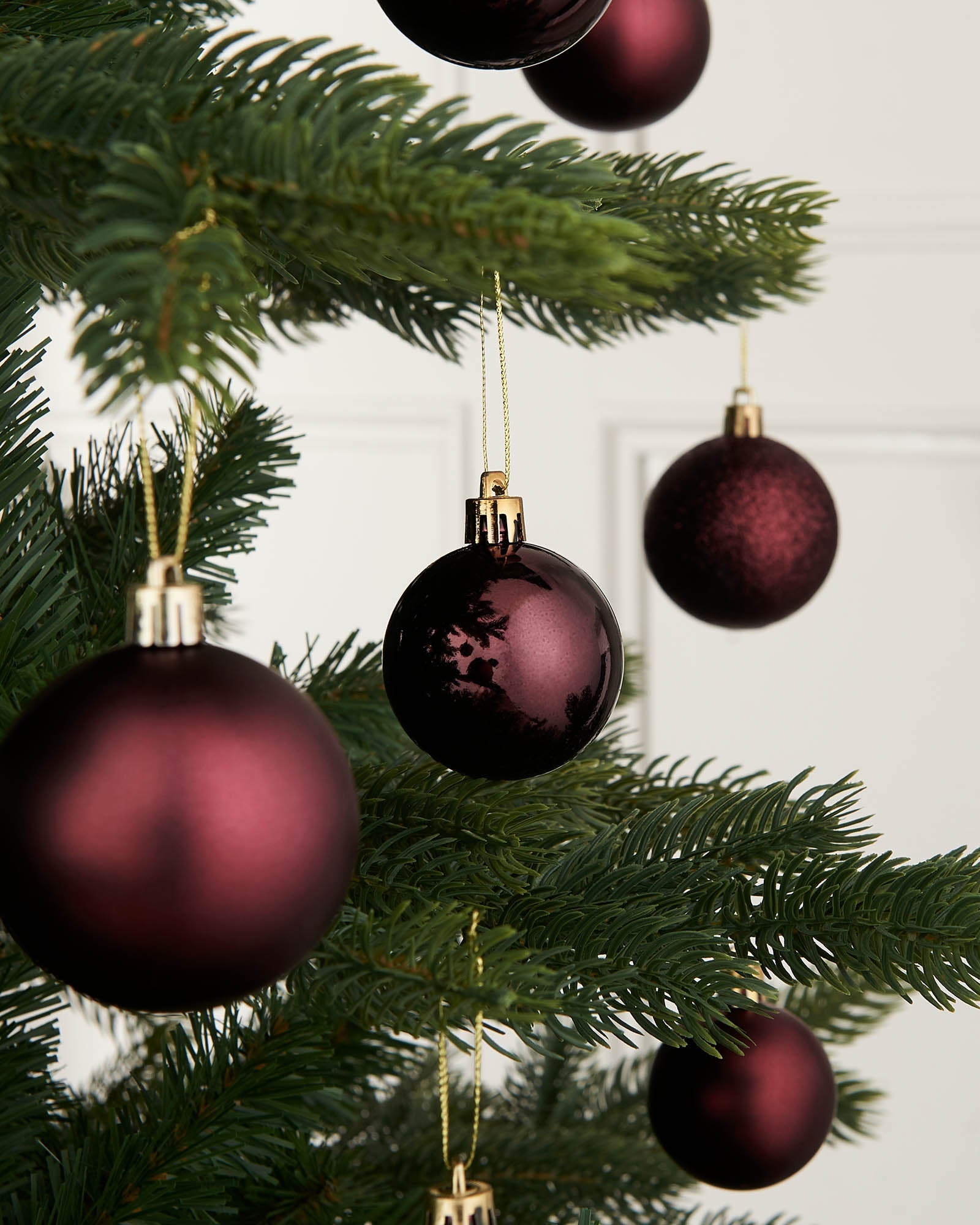 A close-up of several burgundy red Christmas baubles hanging on a Christmas tree, with a focus on their shiny and matte finishes.