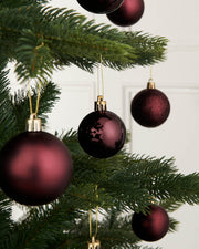 A close-up of several burgundy red Christmas baubles hanging on a Christmas tree, with a focus on their shiny and matte finishes.
