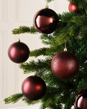 Red round Christmas ornaments hanging on a green Christmas tree.