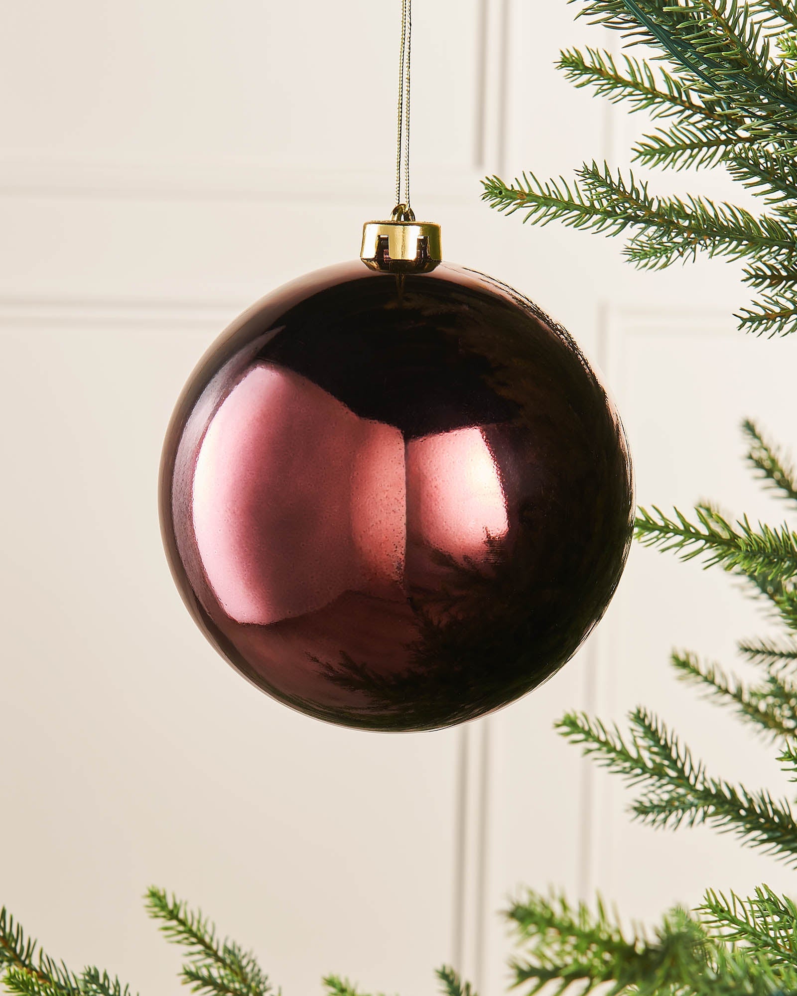 A shatterproof burgundy red bauble hanging from a Christmas tree, with a glossy finish.