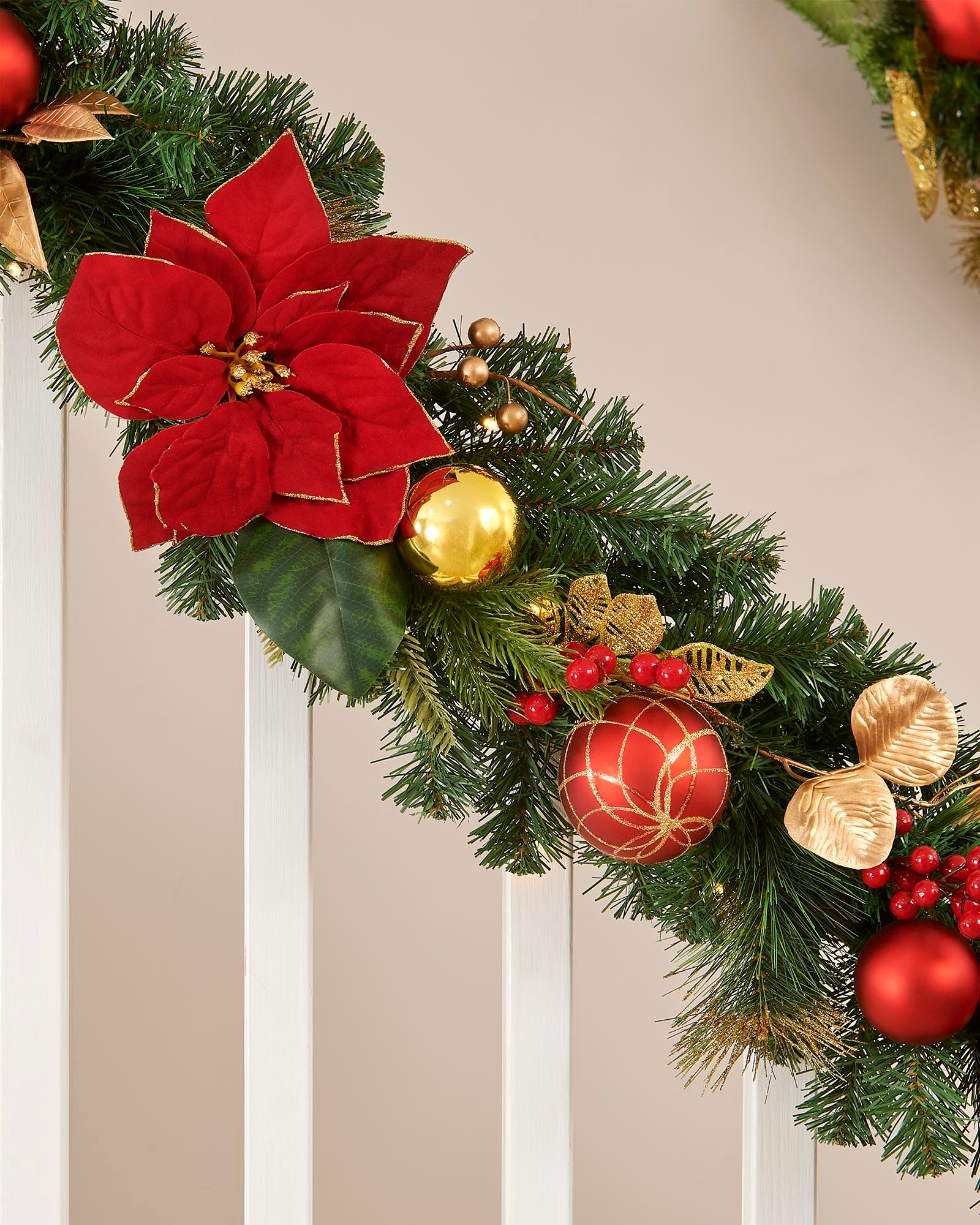 Decorative Christmas garland with red poinsettias, gold leaves, and red balls on a neutral background.