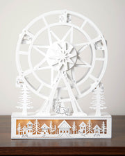 Decorative white ferris wheel with a village scene on a wooden base against a plain background