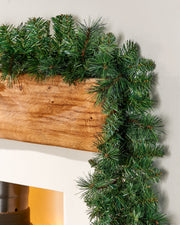 Green pine garland on a wooden mantel above a fireplace.