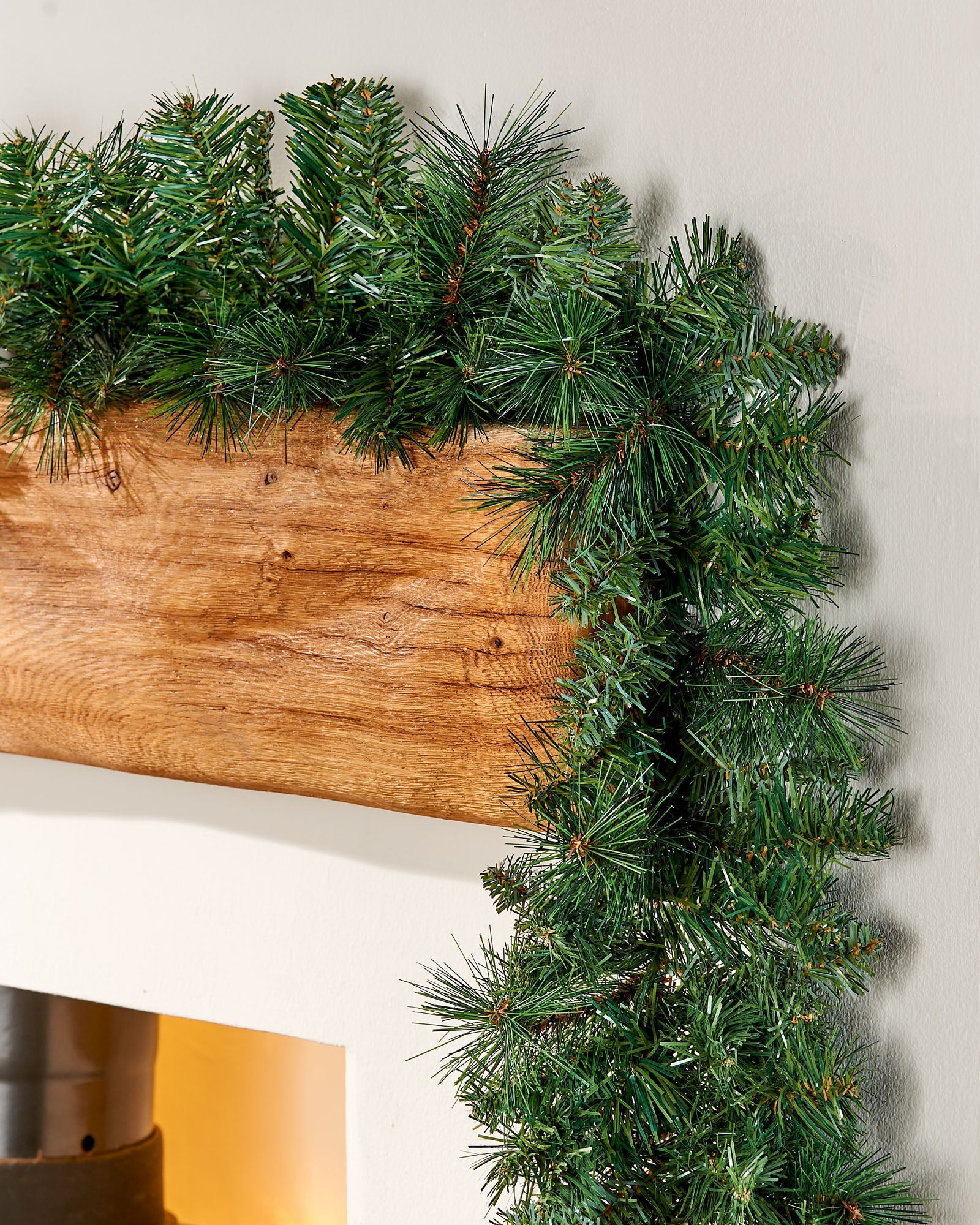 Green pine garland on a wooden mantel above a fireplace.