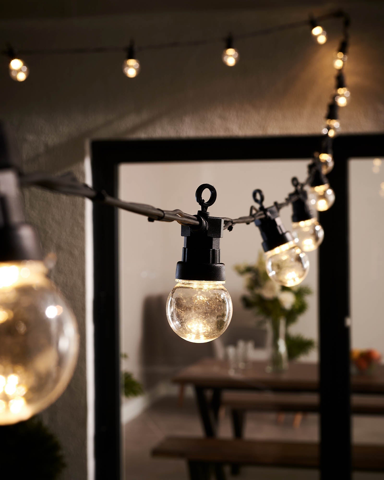 String lights with clear bulb caps and warm white glow, hanging outdoors, with a focus on the lights and a blurred background.