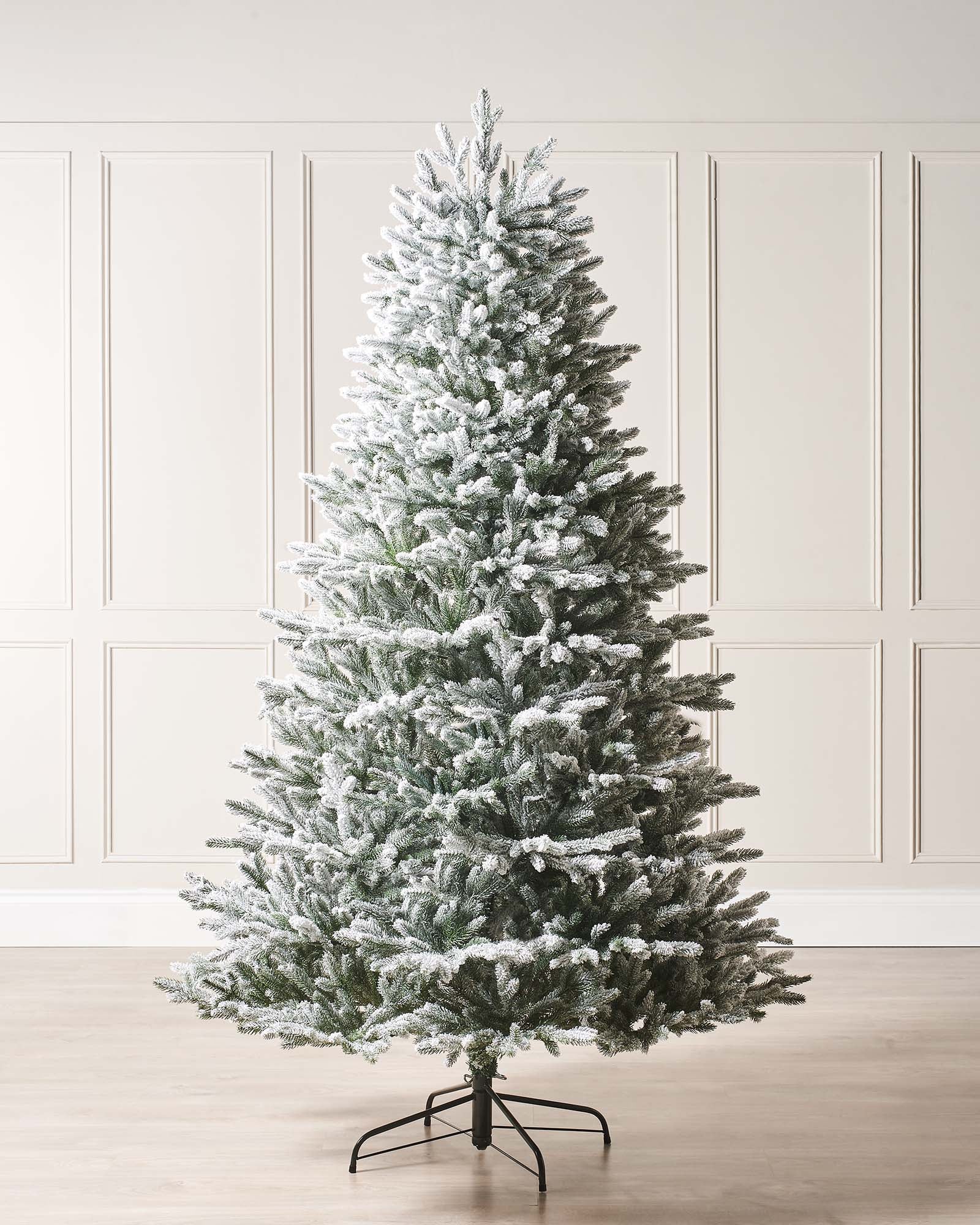 Luxury snow-flocked artificial Christmas tree with soft, snow-dusted tips and a full-bodied, naturalistic shape. Features hinged branches for easy assembly and storage, providing a reusable, elegant centerpiece that captures the charm of a rustic winter wonderland.