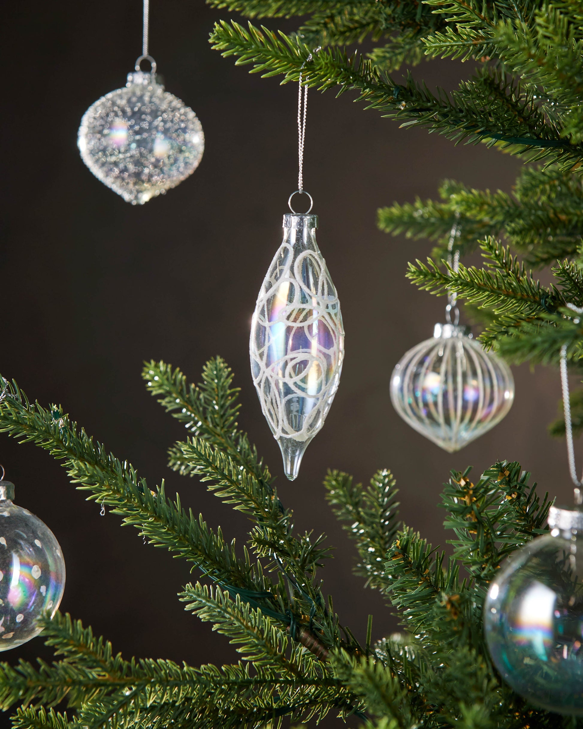 Decorative glass ornaments hanging on a Christmas tree with a dark background