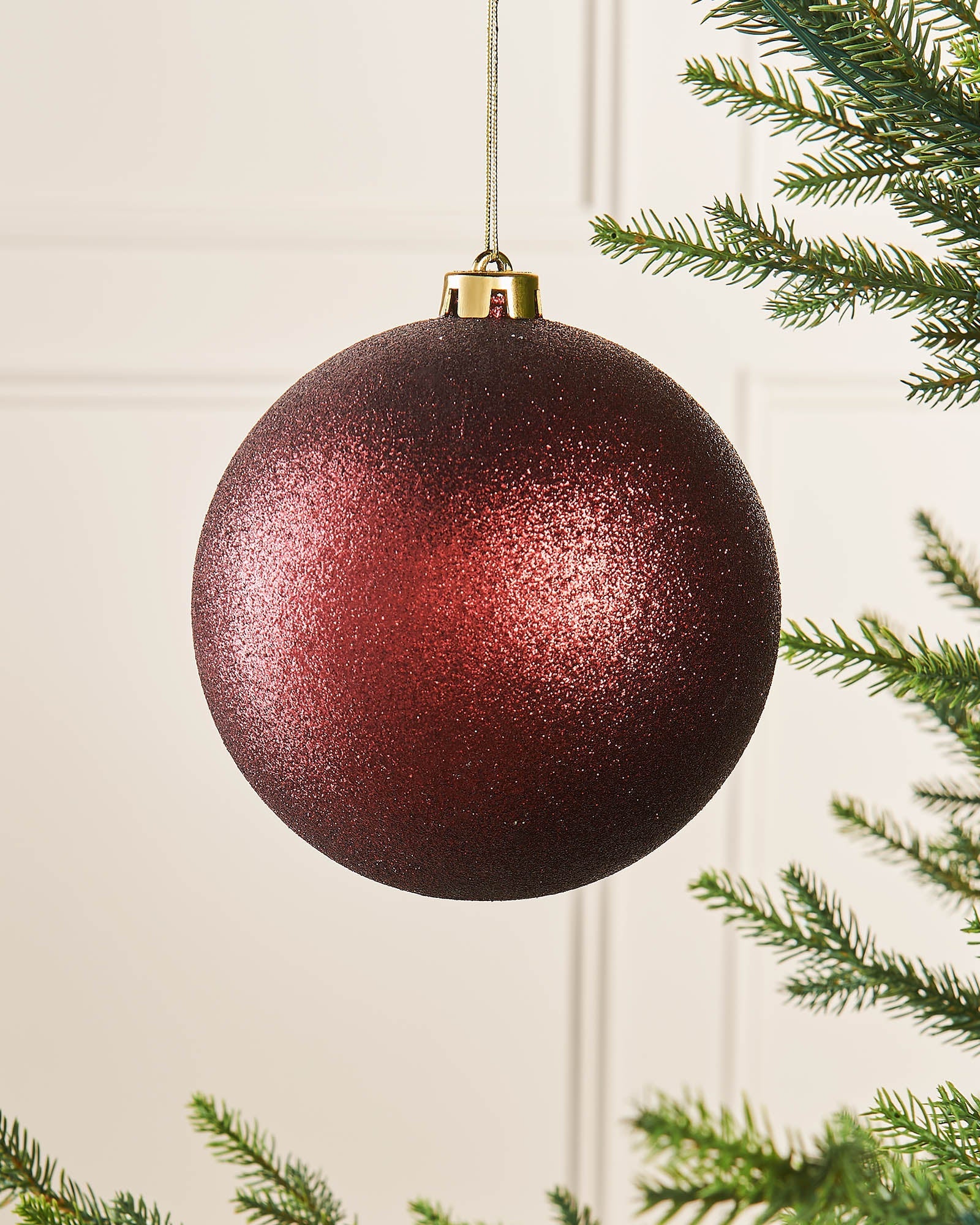 A oversized burgundy glitter shatterproof bauble hanging from a string, designed as a Christmas decoration.