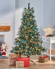 A pre-lit Scandinavian spruce Christmas tree with frosted green PVC branches, warm white LED lights, natural pinecones, and red berries. Positioned in a festive indoor setting with Christmas presents and a seasonal sign, capturing the rustic charm of a snow-dusted Nordic forest.