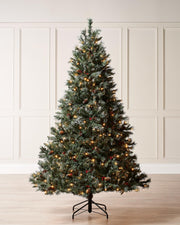 A pre-lit Scandinavian spruce Christmas tree with frosted white-tipped PVC branches, warm white LED lights, natural pinecones, and red berries. Set on a sturdy metal stand, this indoor tree evokes the charm of a snowy Nordic forest.