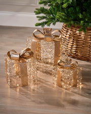 Decorative gift boxes with gold ribbons on a wooden floor next to a Christmas tree.