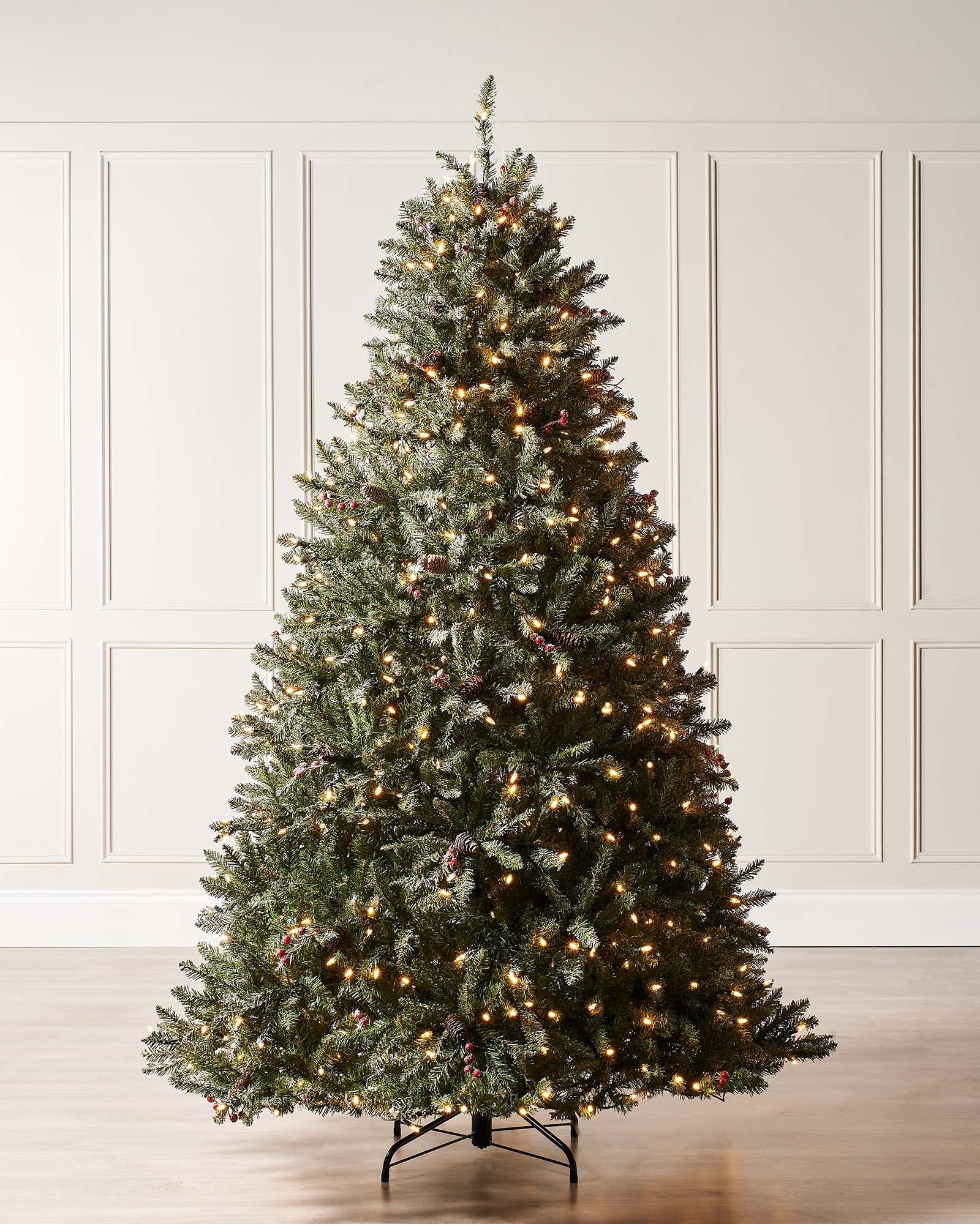 A pre-lit decorated Christmas tree with snow flocked branches, warm white LEDs, and adorned with berries and pinecones, displayed indoors. Pre-lit decorated snow flocked Christmas tree with warm white LED lights, natural-looking berries and pinecones, and 8-function lighting settings—suitable for indoor and outdoor use, featuring a full snowy design for a winter wonderland effect.
