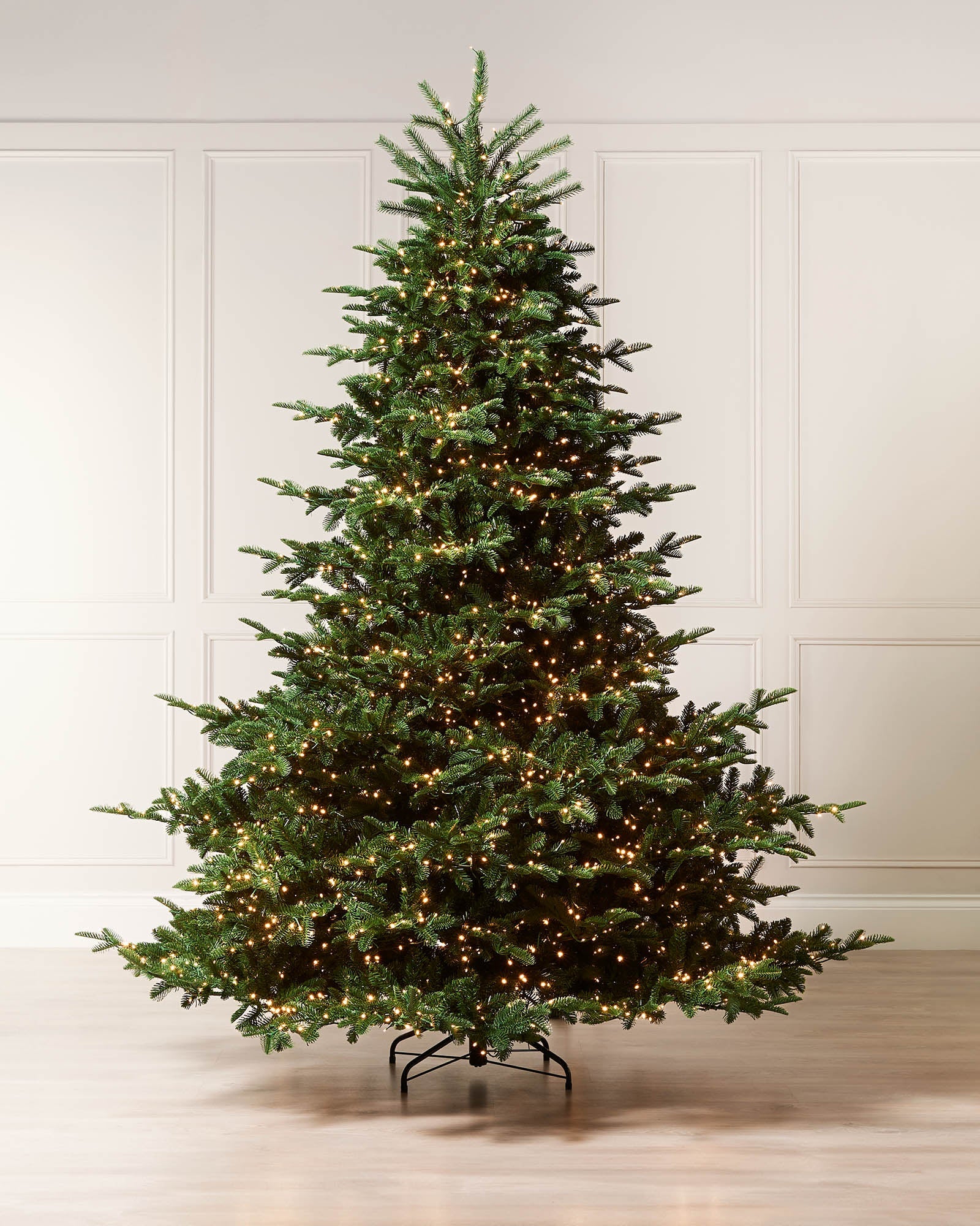 "A 6.5 ft pre-lit Noble Fir artificial Christmas tree with a tiered, natural silhouette and dense mixed PE and PVC foliage. The tree features 2,750 evenly distributed warm-white LED lights, hinged branches for easy setup, and comes with a 5 m lead, external controller with multiple light modes and timer, plus a discreet foot pedal for light control.