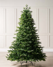 A life-like artificial Christmas tree with green mixed tips on a freestanding metal stand, displayed against a plain background.