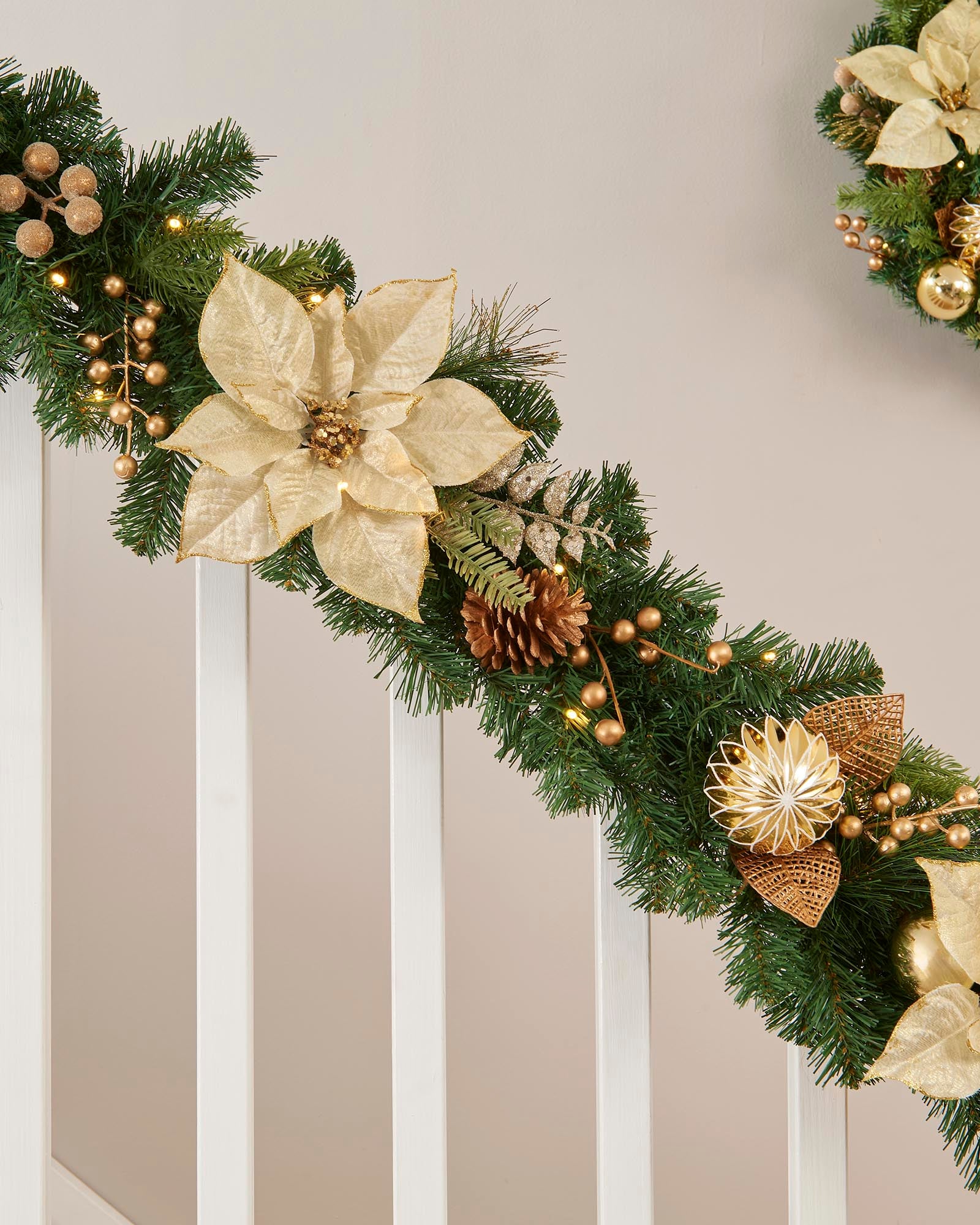 Decorative Christmas garland with gold poinsettias and pinecones on a neutral background