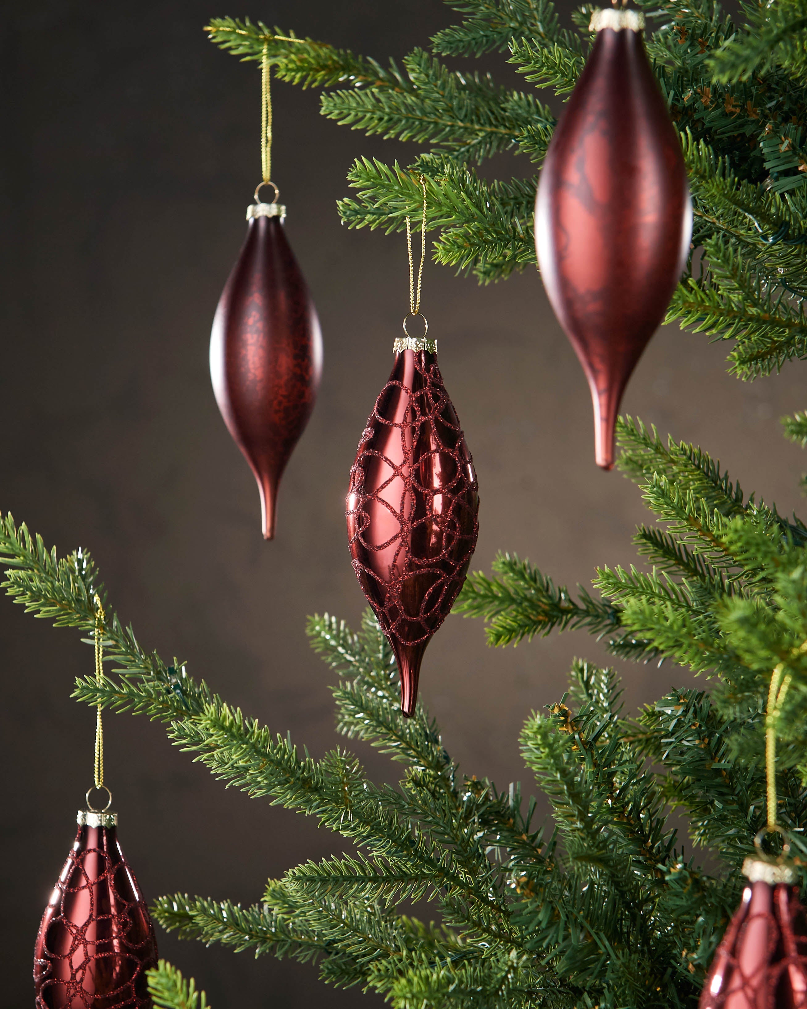 Decorative red ornaments hanging on a Christmas tree with a dark background