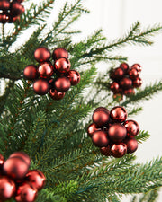 A cluster of burgundy glass berry baubles hanging from green Christmas tree branches.