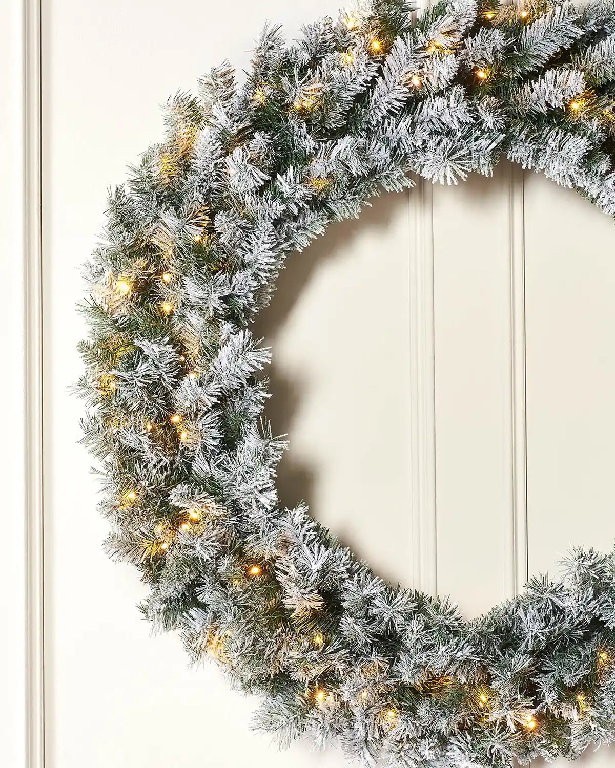 Close-up of 1 m pre-lit snow-flocked majestic wreath on a lifestyle wall